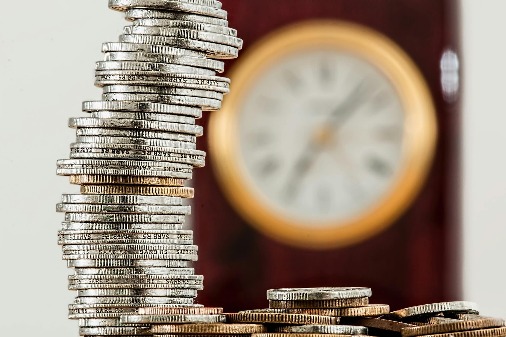 Stacked coins in front of a clock