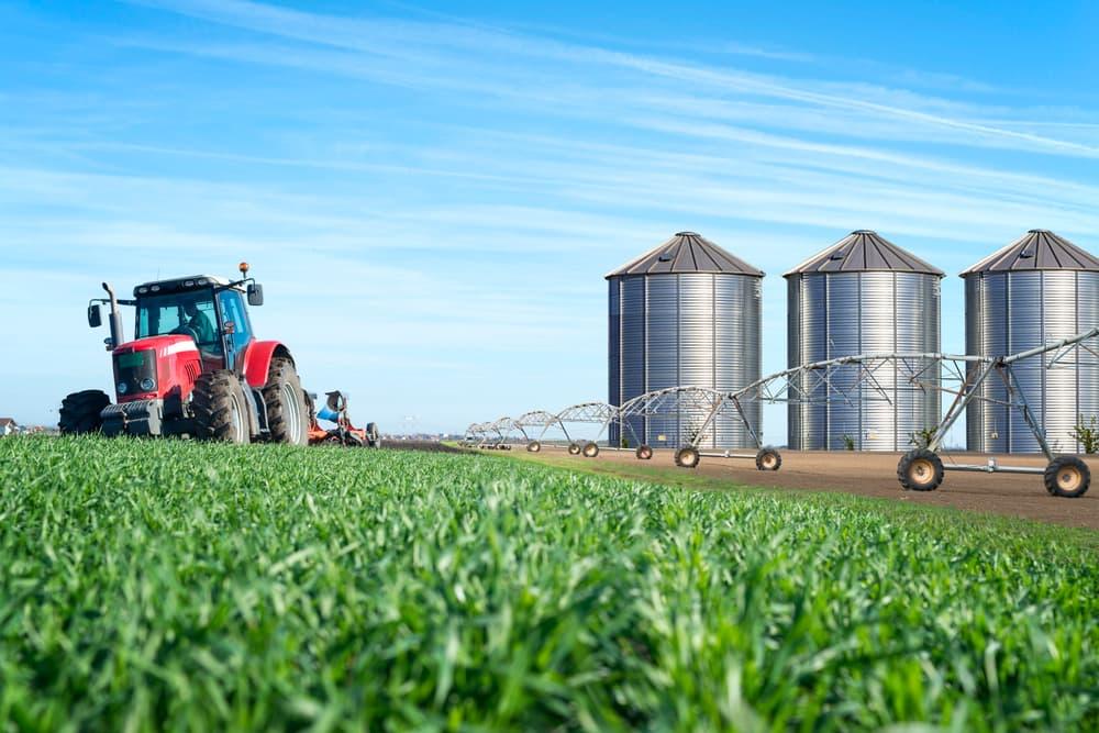 Tractor in a field beside grain silos