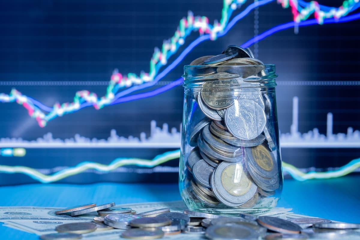 Coins in a glass jar in front of a rising market chart